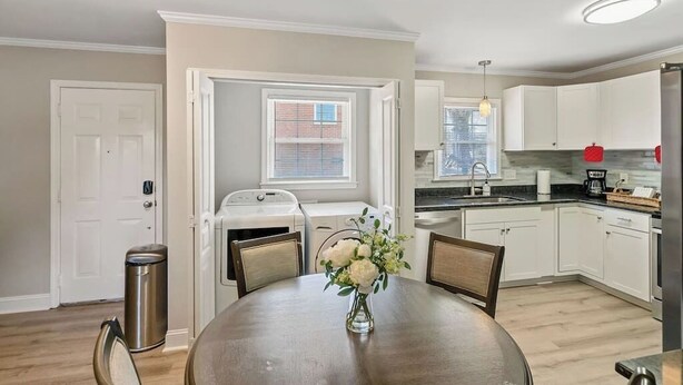 A modern kitchen with white cabinets, a dining table with chairs, and a small window.
