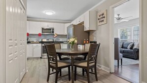 A kitchen with white cabinets, a dining table with chairs, a refrigerator, and a ceiling fan.