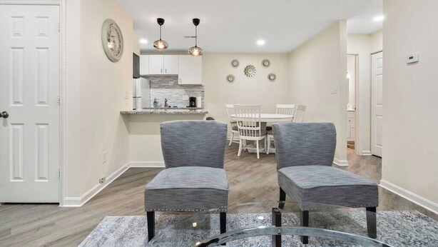 A modern kitchen with white cabinets, a granite countertop, and a dining area with a white table and chairs. - 2BR Escape | Hot Tub | Parking 4 Cars | Pineville (Charlotte)