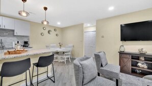 A modern kitchen with a dining area, bar stools, a flat-screen TV, and a fireplace. - 2BR Escape | Hot Tub | Parking 4 Cars | Pineville (Charlotte)