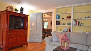 A living room with a wooden cabinet, a gray sofa, a coffee table, and a bookshelf. - The Captain John Butman House (Rockport)