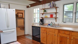 A kitchen with wooden cabinets, a refrigerator, a dishwasher, and a window with a view of the outside. - The Captain John Butman House (Rockport)