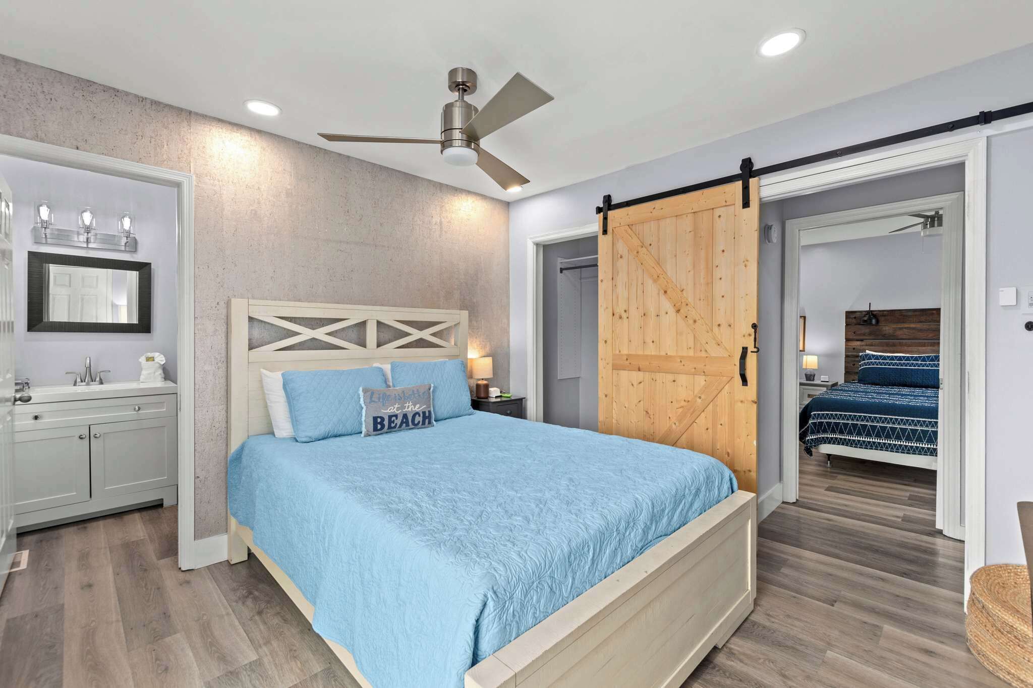 A bedroom with a bed, a ceiling fan, a wooden door, and a bathroom with a sink and mirror.