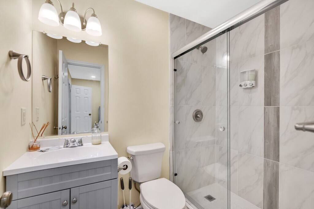 A bathroom with a shower, toilet, sink, and mirror.