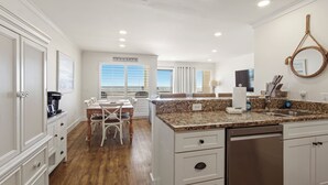 A modern kitchen with granite countertops, white cabinetry, and a dining area with white chairs.