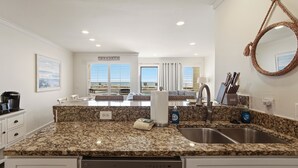 A kitchen with granite countertops, a stainless steel sink, and a large mirror.