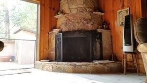 A stone fireplace with a black TV on a wooden stand, a wooden ceiling, and a view of the outside. - Bear’s Lair Cabin, Willow Cove, Bass Lake (Bass Lake)