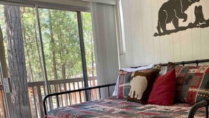 A bedroom with a bed, a bear wall decal, and a view of trees through the window. - Bear’s Lair Cabin, Willow Cove, Bass Lake (Bass Lake)