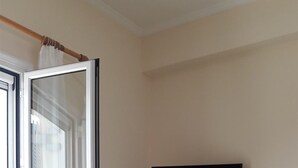 Habitació amb porta corredissa de vidre, televisió plana penjada a la paret i una butaca color beix.