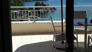 Un balcó amb vista al mar, una taula, cadires i un parasol gran.