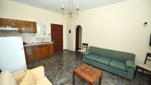 A living room with a sofa, a coffee table, and a kitchen area with cabinets and a refrigerator. - 03 | Sea View - One Bedroom Apartment (Palaiokastritsa)