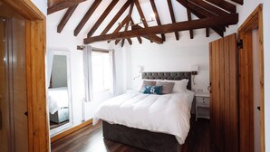 A bedroom with a large bed, wooden beams on the ceiling, a bedside table, and a nightstand. - Flint Cottage - Sleeps 6 - Private Woodland (Hailsham)