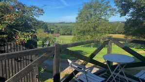 A wooden deck with a table and chairs overlooking a green landscape with trees and a fence. - Flint Cottage - Sleeps 6 - Private Woodland (Hailsham)