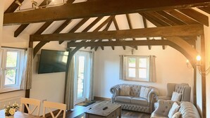 A cozy living room with a wooden ceiling, a sofa, a chair, and a coffee table. - Flint Cottage - Sleeps 6 - Private Woodland (Hailsham)