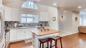 Una cocina moderna con armarios blancos, encimera de mármol y una isla de madera con taburetes de bar.