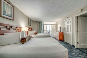 Two large beds with white linens and wooden headboards, a dresser, and a television.