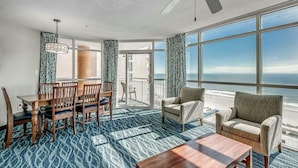 A room with a dining table and chairs, a sofa, a coffee table, and large windows offering a view of the ocean. - · NEW! Stunning Oceanfront Condo -Amazing Water Amenities! (Myrtle Beach)