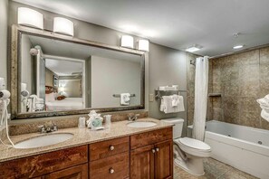 A bathroom with a large mirror, two sinks, a toilet, and a bathtub.