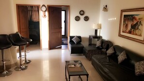 A living room with a sofa, two chairs, a coffee table, a lamp, and a painting on the wall. - Eden Appartment in Lahore (Lahore)
