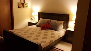 A bed with a patterned bedspread, two bedside tables with lamps, and a door. - Eden Appartment in Lahore (Lahore)
