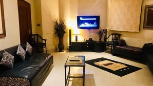 A living room with a sofa, armchairs, a coffee table, a TV, and a fireplace. - Eden Appartment in Lahore (Lahore)