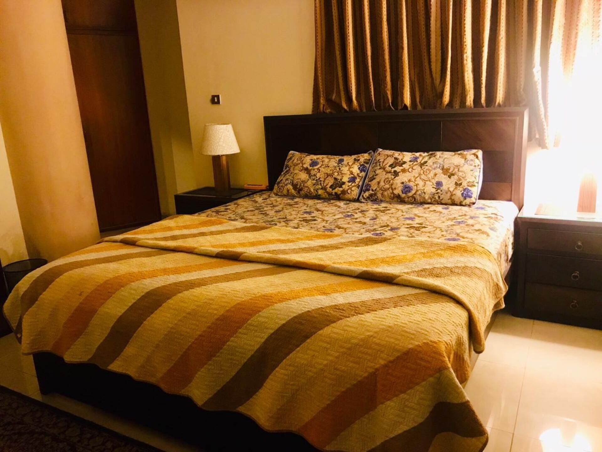 Una habitación de hotel con una cama grande, una mesita de noche con lámpara y una ventana con cortinas.