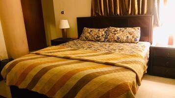Una habitación de hotel con una cama grande, una mesita de noche con lámpara y una ventana con cortinas.