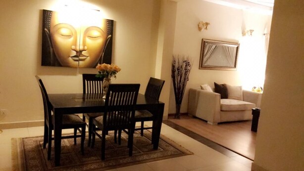 A dining area with a table and chairs, a vase with flowers, and a Buddha painting on the wall. - Eden Appartment in Lahore (Lahore)