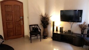 A living room with a wooden door, a black chair, a decorative vase, a television on a stand, and a lamp. - Eden Appartment in Lahore (Lahore)