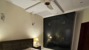 A bedroom with a bed, a wardrobe, a ceiling fan, and a nightstand with a lamp.