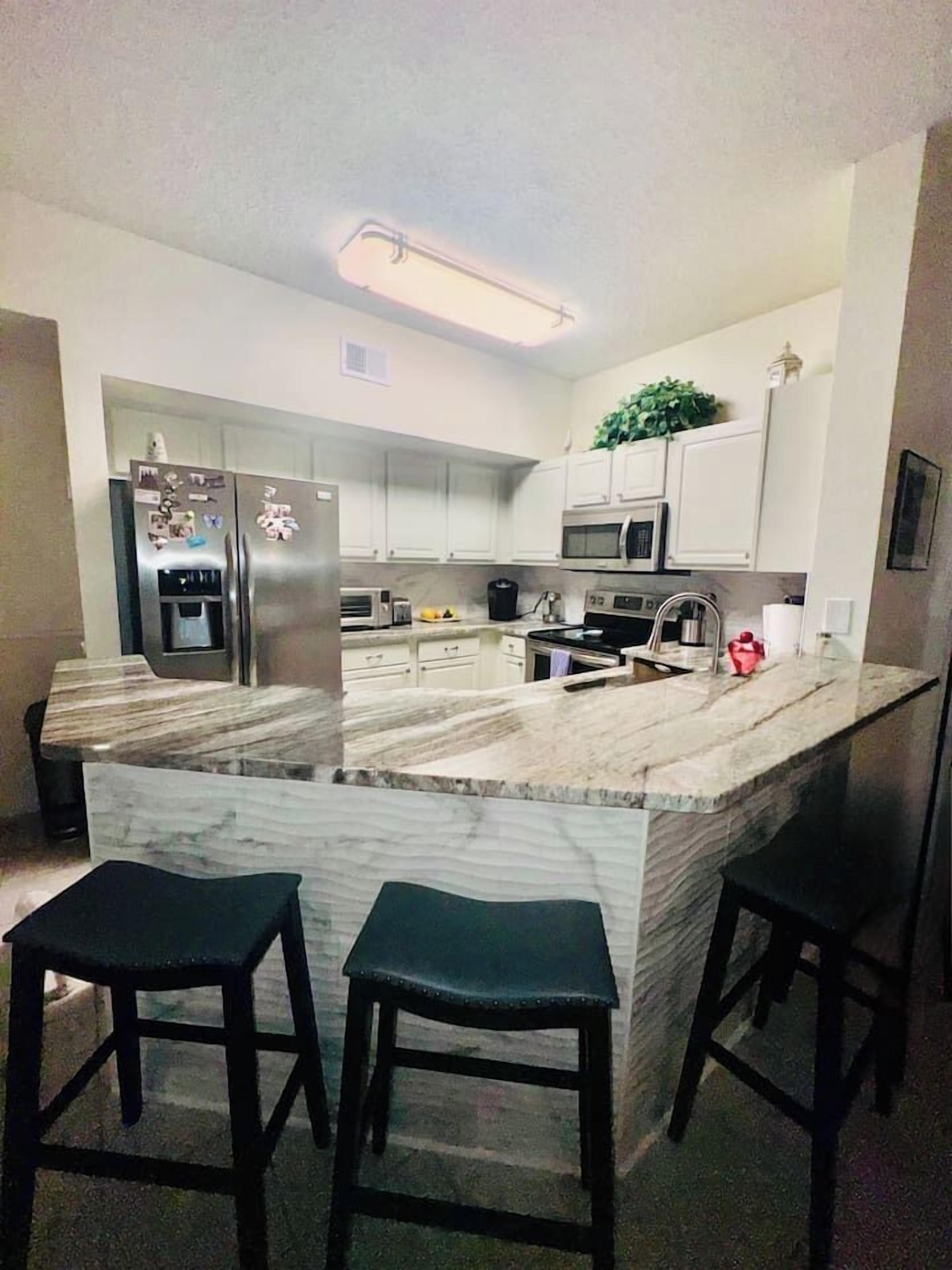 A modern kitchen with a marble island, stainless steel appliances, and black bar stools.