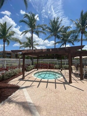 Un área de piscina con una pérgola, palmeras y una valla blanca.