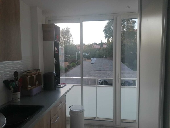 A kitchen with a large window, a trash bin, and a view of a street and parked cars.