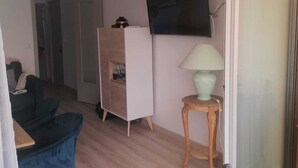 Habitación con sofá, una mesita de noche con lámpara, televisor montado en la pared y puerta corrediza de vidrio que da a un espacio exterior.