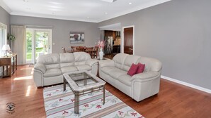 A spacious living room with a beige sectional sofa, a glass coffee table, and a patterned rug.