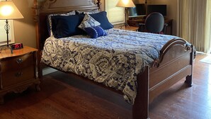 A bedroom with a wooden bed, two bedside lamps, a ceiling fan, a TV, and a window with curtains.