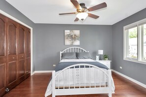 A bedroom with a white bed, grey walls, a ceiling fan, and a window. - Great place to stay in Warrenville (Warrenville)