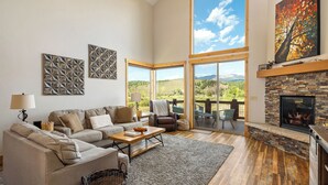 Ein geräumiges Wohnzimmer mit einem großen Sofa, einem Kamin und Blick ins Freie.