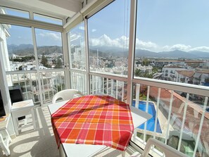 Ein Balkon mit Tisch und Stühlen, einer karierten Tischdecke und Blick auf Stadt und Berge.