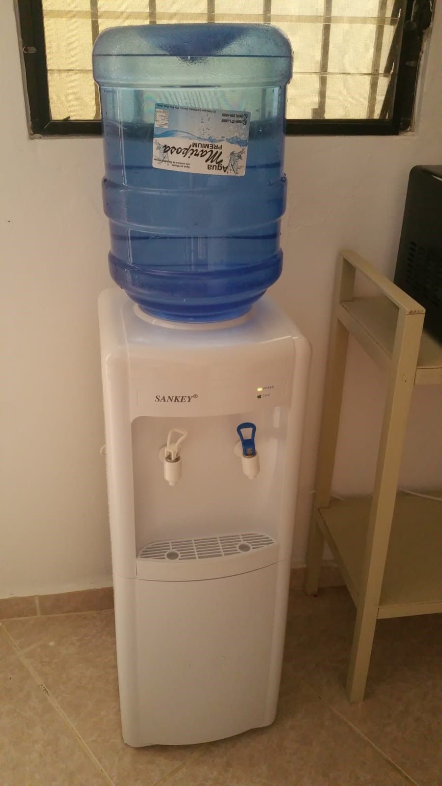 A water dispenser with a large blue water jug on top, a power button, and a cold water tap.