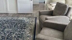 Un salon avec un canapé gris, un tapis à motifs, une porte coulissante de style rustique et une œuvre d’art encadrée accrochée au mur.