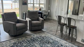 Een ruime woonkamer met een groot tapijt, twee fauteuils, een eettafel met stoelen en uitzicht op een meer door grote ramen.
