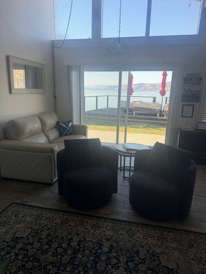 A living room with a sofa, two armchairs, a patterned rug, and a view of a lake through a glass door.