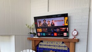 Una sala de estar con chimenea, un televisor de pantalla plana montado encima y una silla Adirondack blanca, además de un tapete estampado.