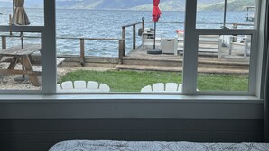 Vista desde una habitación con ventanas amplias que dan a una terraza con mobiliario exterior y un paraguas rojo.