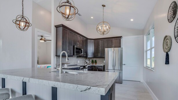 A modern kitchen with dark wood cabinets, stainless steel appliances, and a marble island with bar seating.