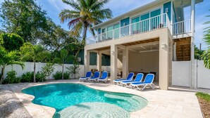 A pool with blue lounge chairs, a covered patio, and a two-story building with a balcony.