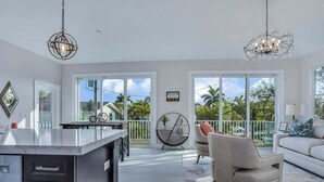 A spacious living area with a kitchen, large windows, and a balcony with a view of palm trees.