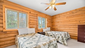 Une chambre de style rustique avec deux lits, des murs en bois, un ventilateur de plafond et de grandes fenêtres.