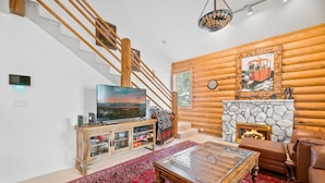Un salon avec une cheminée en pierre, un téléviseur, un escalier en bois et un tapis rouge à motifs.